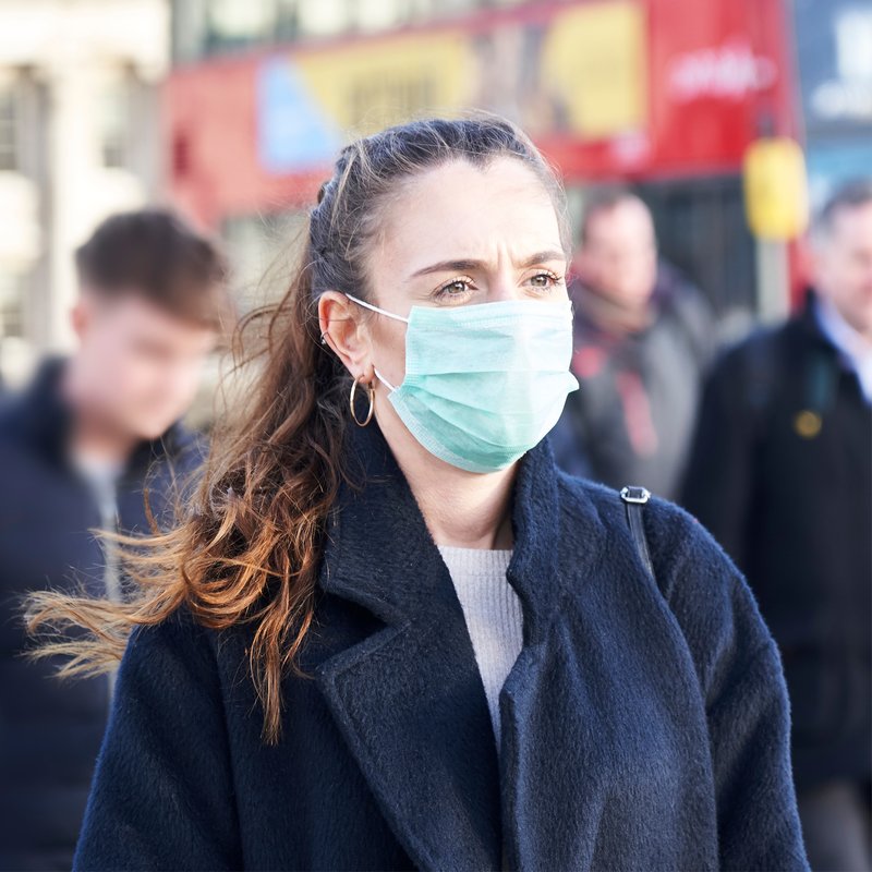 una mujer llevando mascarilla en una calle con más gente
